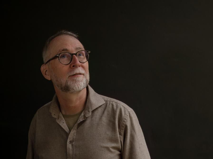 Mand med briller der står foran en mørk baggrund og kikker opad